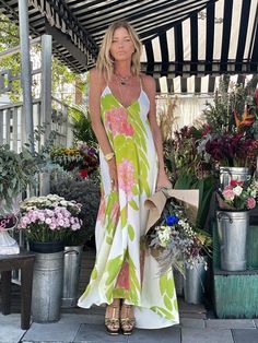 a woman is standing in front of some potted plants and wearing a dress with flowers on it