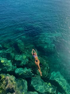 a woman is swimming in the ocean with clear blue water and green algae on the rocks