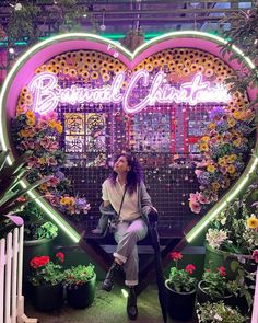 a woman sitting on a bench in front of a heart - shaped display with flowers