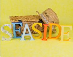 the word seaside spelled with letters in front of a basket and hat on yellow background