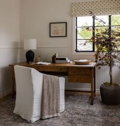 a room with a desk, chair and potted plant in the corner next to it