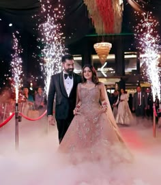 a man and woman in formal wear standing next to each other with fireworks behind them