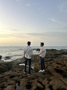 two people standing on rocks near the ocean