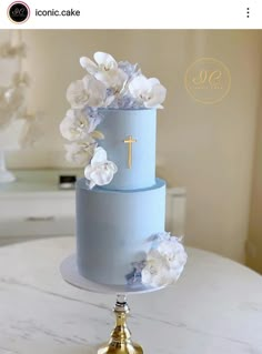 a blue cake with white flowers and a cross on top is sitting on a table