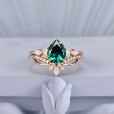 a ring with an emerald colored stone surrounded by white and rose gold diamonds on top