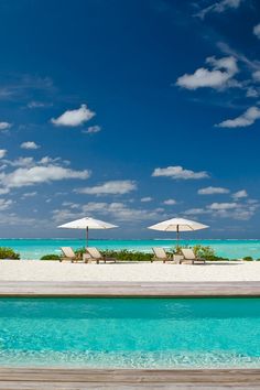 lounge chairs and umbrellas sit on the beach near an ocean pool with clear blue water