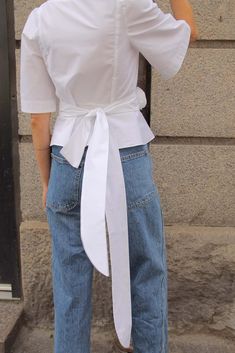 a woman in jeans and a white shirt is talking on her cell phone while standing next to a building