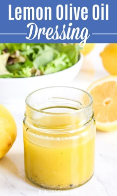 a mason jar filled with lemon olive oil sitting next to a bowl of salad and two lemons