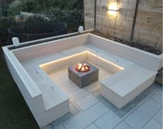 a fire pit in the middle of a patio with benches around it and lights on