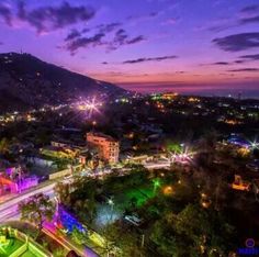 an aerial view of a city at night with lights on the buildings and mountains in the background