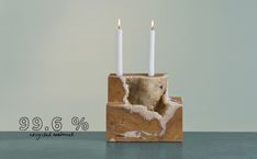 two white candles sitting on top of a stone block with the words 99 6 % written below it