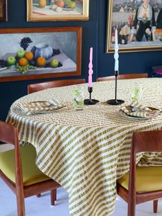 a dining room table with two candles on it and some fruit in the back ground