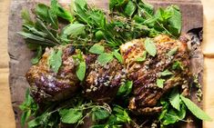 two steaks covered in herbs sit on a cutting board next to some green leaves