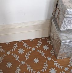 a silver box sitting on top of a wooden floor next to a white flowered wall