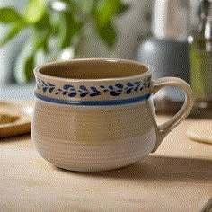 a white and blue coffee cup sitting on top of a wooden table next to a potted plant