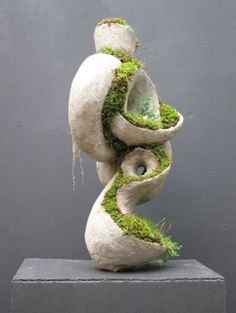 a sculpture with moss growing out of it's sides and in the shape of a spiral