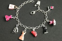 A collection of silver plated and colorfully enameled fashion themed charms have been dispersed around a shimmering silver plated bracelet chain in this handmade charm bracelet. This fashion charm bracelet is then completed with a lobster clasp and a 1/2 inch of chain at the end for adjustable sizing. Charms in this bracelet include three enameled pink dress charms, an enameled black dress charm, two enameled shoe charms, two enameled purse charms, and a detailed corset charm. ● Sizing ● To dete Trendy Silver Enamel Jewelry, Trendy Nickel-free Silver Charms, Handmade Metal Charm Bracelet For Parties, Trendy Silver Charm Bracelet With Removable Charms, Trendy Silver Bracelet Charms, Trendy Silver Bracelets With Removable Charms, Silver Enamel Jewelry With Dangling Charms, Silver Charm Bracelets As Fashion Accessory, Silver Charms Bracelet As Fashion Accessory