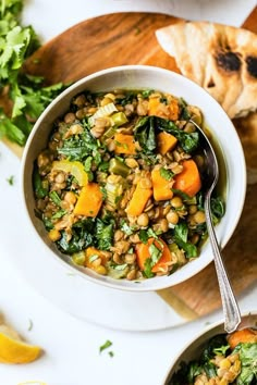 two bowls filled with lentils, carrots and greens next to bread on a cutting board