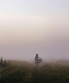 a woman in a white dress is walking on a foggy path through the grass