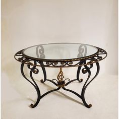 a glass and metal coffee table with an ornate design on the top, against a white background