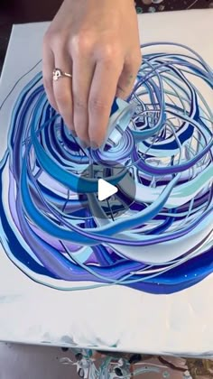 a person is using scissors to cut something out of paper with blue and white swirls