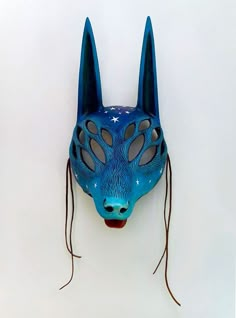 a blue mask with ears and eyes is hanging on a white wall in the shape of a wolf's head