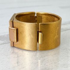 Vintage Monet All That Jazz Cuff Bracelet - Matte Bloomed Gold - Stained Glass Look -Post Modernist design in matte gold finish with inset iridescent glass under a geometric open work design. This great cuff measures 1 1/16 of an inch wide and weighs 3 ounces. It is nice and substantial, beautifully made. It is oval-shaped and measures 1 3/4 inches front to back by 2 1/4 inches side to side (inner measurement). The top panel measures 1 5/8 of an inch by 1 1/16 of an inch. The condition is very good overall with light wear to the surface consistent with age. Gold Brass Modern Bangle, Modern Gold Brass Bangle, Gold Modernist Cuff Bracelet For Formal Occasions, Modernist Gold Bangle Bracelets, Modern Brass Cuff Bangle, Modernist Metal Cuff Bangle, Modernist Gold Metal Cuff Bracelet, Modernist Metal Bangle For Formal Occasions, Formal Modernist Metal Bangle