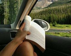 a person reading a book in the back seat of a car with mountains in the background