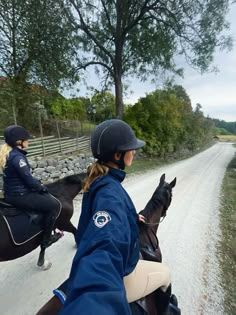 two people riding horses down a dirt road