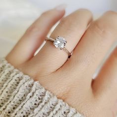 a woman's hand with a diamond ring on top of her finger and a sweater