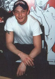 a young man sitting in front of a wall with tattoos on it's arms