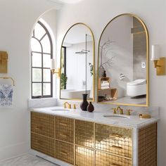 a bathroom with two mirrors and gold accents on the vanity, along with a white toilet