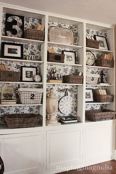 a living room filled with lots of white bookshelves covered in pictures and baskets