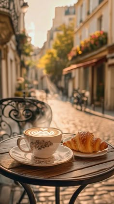 a cup of coffee and a croissant on a table in front of some buildings