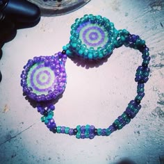 two purple and green beaded necklaces sitting on top of a table