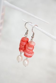 Introducing our exquisite Coral Stone & Big Freshwater Pearl Earrings, a captivating blend of elegance and craftsmanship. Handcrafted with precision using high-quality stainless steel, these unique earrings are a testament to meticulous artistry and attention to detail. The earrings feature a carefully curated selection of natural stones, adding a touch of authenticity to their design. Multiple stones are delicately threaded, creating a visually stunning composition. What makes these earrings truly stand out is the dangling freshwater pearl bead, elegantly swaying like a drop of liquid silver. With a length of 5.7cm (2.2 inches), these earrings are perfectly balanced, making them a versatile accessory suitable for various occasions. The combination of coral stone and freshwater pearl exude Coral Wedding Earrings, Pearl White Mother Of Pearl Dangle Earrings, Coral Beaded Earrings For Gifts, Pearl Drop Mother Of Pearl Dangle Earrings, Coral Pearl Drop Jewelry Gift, Coral Pearl Jewelry Gift, Handmade Coral Drop Earrings, Handmade Pearl White Dangle Pearl Earrings, Coral Pearl Drop Jewelry As Gift