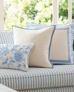 blue and white pillows on a striped couch in front of a window with trees outside