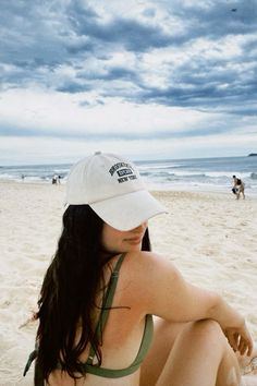 a woman sitting on top of a sandy beach next to the ocean under a cloudy sky