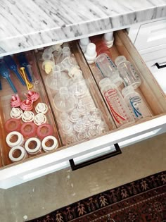 an open drawer filled with lots of plastic bottles and other items on top of a counter