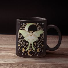 a black coffee mug with an image of a butterfly on it's wings and moon phases