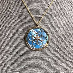 "Seed of Life pendant 24 carat gold plated on 925 Silver, blue mother of pearl and crystal. The symbol commonly referred to as the Seed of Life is made up of seven circles; one in the center, and six others placed around it according to ancient spiritual traditions. It's tought that the seven interlocking circe are compared to the seven days of creation, with the different circles being ascribed to different points in the universe's making. The flore blooming in the middle is considered the Cons Gold Mother Of Pearl Necklace With Gemstone, Gold Mother Of Pearl Flower Pendant Jewelry, Gold Necklace With Gemstone And Mother Of Pearl, Gold Necklaces With Gemstone And Mother Of Pearl, Spiritual Round Mother Of Pearl Jewelry, Spiritual Round Mother Of Pearl Necklace, Gold Star Of David Gemstone Jewelry, Gold Star Of David Jewelry With Gemstone, Spiritual Blue Gold-plated Jewelry