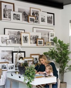 a woman sitting at a desk with a child in front of her and pictures on the wall behind her