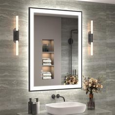 a bathroom with a sink, mirror and lights on the wall next to flowers in a vase