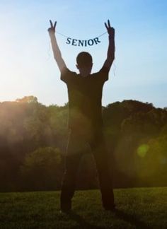 a man standing in the grass with his hands up and holding a string that says senior