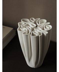 a white vase sitting on top of a black table next to a book and pen