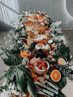 an arrangement of fruits and vegetables on a table with greenery, flowers and leaves