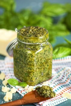 a jar filled with pesto next to a wooden spoon on top of a table