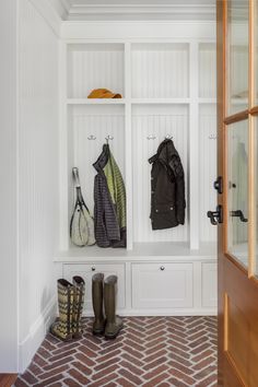 two coats and boots are hanging on the wall in this mud room with brick flooring