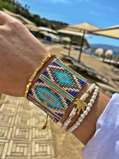 a woman's arm with three bracelets on it and an umbrella in the background