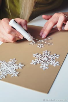 a woman is cutting out snowflakes on a piece of paper with a marker